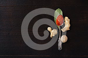 Spoon of chili powder surrounded with bay leaf, ginger and nutmeg on black wooden surface