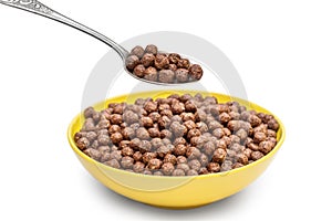 Spoon with chocolate cereal balls over bowl with cereal balls on white