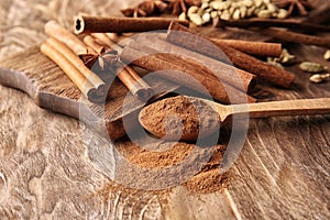 Spoon with cinnamon powder and sticks on wooden background