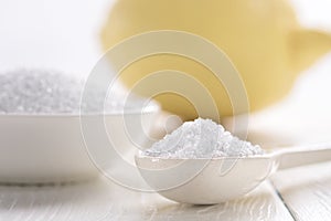 Spoon with citric acid and lemon on a white wooden table