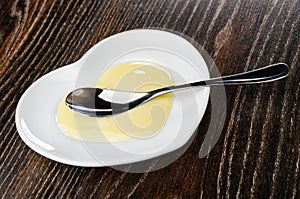 Spoon, condensed milk in white saucer in heart shape on wooden table