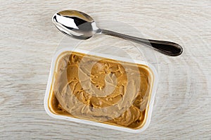 Spoon, container with peanut butter on wooden table. Top view
