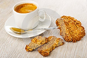 Spoon, cup with coffee on saucer, pieces of cookie, oat cookies with peanut on wooden table