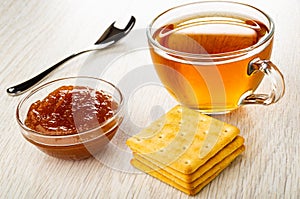 Spoon, cup with hot tea, bowl with apple jam, crackers on wooden table