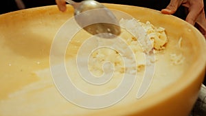 spoon delicately scrapes against a luscious cheese wheel.