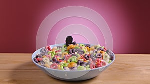 Spoon falls into deep bowl filled with multicolored corn rings and milk. Flakes and splashes of milk fly in different