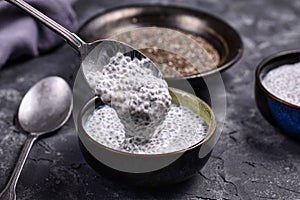 Spoon filled with chia seed pudding made with dry seeds soaked in milk in small bowls