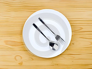 A spoon and a fork on empty white plate on a wooden table