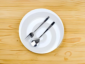 A spoon and a fork on empty white plate on a wooden table