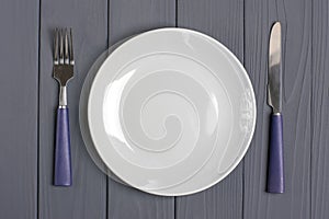 Spoon, fork, grey plate on a gray wooden background Table setting concept