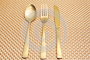 Spoon, fork, knife gold color isolated on gold color background. Top view. Close-up