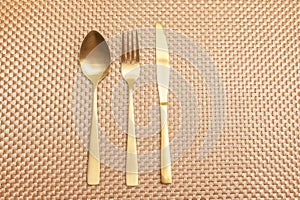 Spoon, fork, knife gold color isolated on gold color background. Top view. Copy space. Horizontal shot