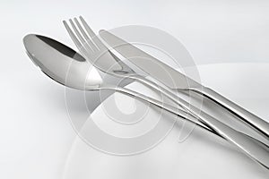 Spoon, fork and knife on white empty plate