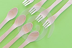 Spoon and forks setup Cutlery on a bright green background. Eco-friendly wooden disposable cutlery on bright colored backdrop.