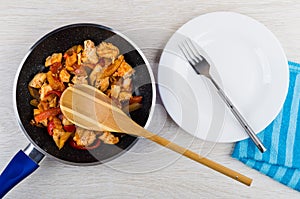 Spoon in frying pan with meat, sweet pepper, plate, fork