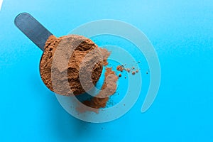 A spoon full of chocolate flavor whey protein powder top view with copy space, blue background