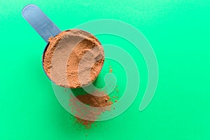 A spoon full of chocolate flavor whey protein powder, top view with copy space, green background