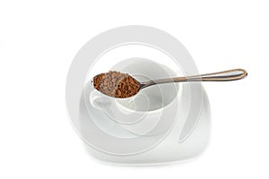 Spoon full of granulated instant coffee over empty white cup and saucer.