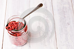 A spoon an full jar of superfood goji berries on white wood table