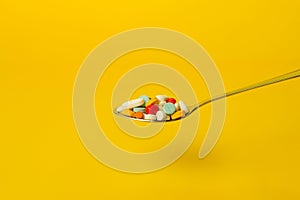 Spoon full of pills on a yellow background