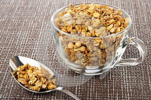 Spoon with granola, muesli in transparent cup on dark mat