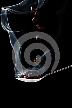 Spoon with hot coffee beans with smoke on a black background with falling coffee beans