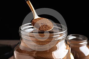 Spoon of instant coffee over jar against black background