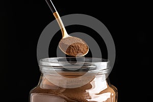 Spoon of instant coffee over jar against black background