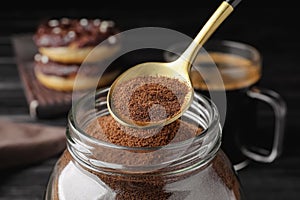 Spoon of instant coffee over jar on black table, closeup