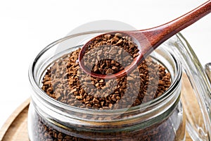 Spoon of instant coffee over jar on table, closeup