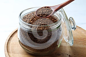 Spoon of instant coffee over jar on white table, closeup