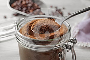 Spoon of instant coffee over jar on white table, closeup