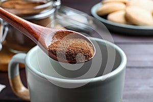 Spoon of instant coffee over mug on table, closeup