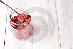 A spoon on a jar filled with superfood goji berries on white wood