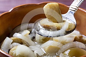 Spoon with marinaded mushroom and onion over pot with mushrooms