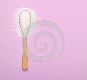A spoon with natural sweetener lies on a pink background