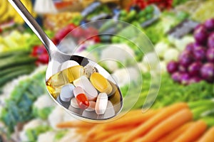 Spoon with pills, dietary supplements on vegetables background