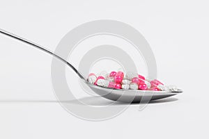 Spoon with pink pills on a white background. Drug overuse and antibiotic resistance