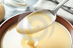 Spoon of pouring condensed milk over bowl, closeup.