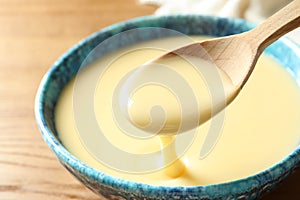 Spoon of pouring condensed milk over bowl on table, closeup.