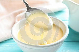 Spoon of pouring condensed milk over bowl on table, closeup