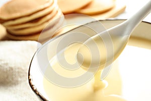 Spoon of pouring condensed milk over bowl on table, closeup with space for text.