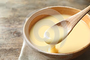 Spoon of pouring condensed milk over bowl on table, closeup with space for text.