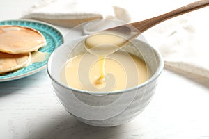 Spoon of pouring condensed milk over bowl on table. Dairy products