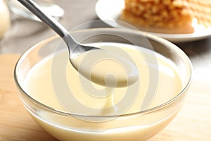 Spoon of pouring condensed milk over bowl on table. Dairy products