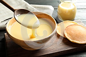 Spoon of pouring condensed milk over bowl on table, space for text