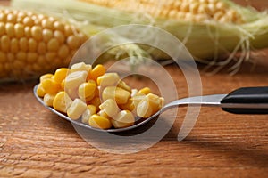 Spoon of preserved corn on wooden table, closeup