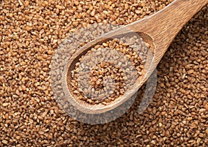 Spoon with raw organic healthy brown bulgur seeds.Macro