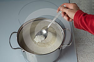 A spoon with rice in a woman's hand over a pot of boiling rice.