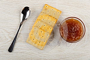 Spoon, row of crackers, bowl with apple jam on wooden table. Top view